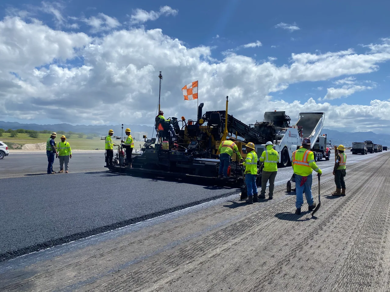 Runway 8L paving crew working beside an asphalt paver in daylight.