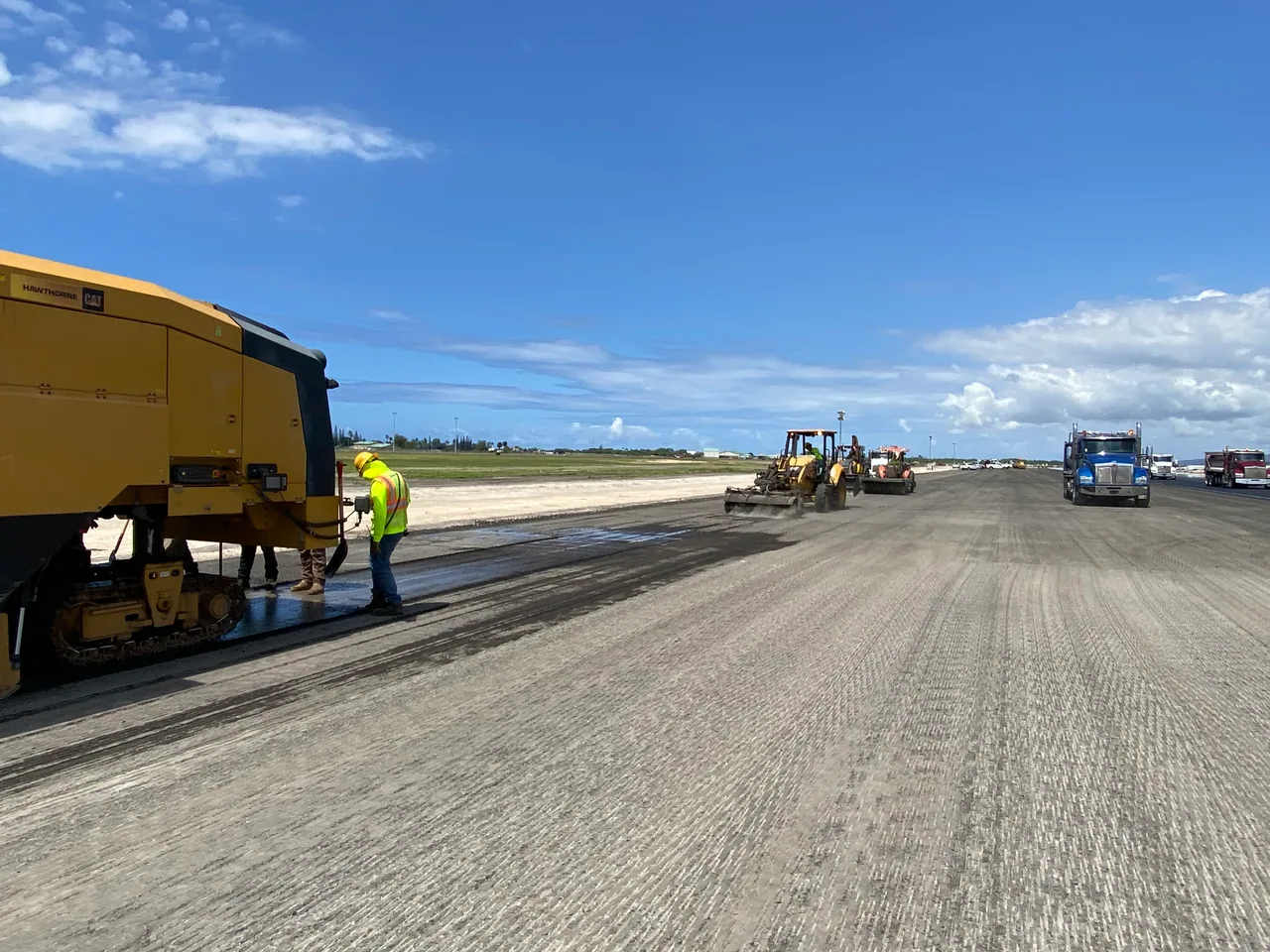 Milling equipment and trucks on the runway during daylight operations.