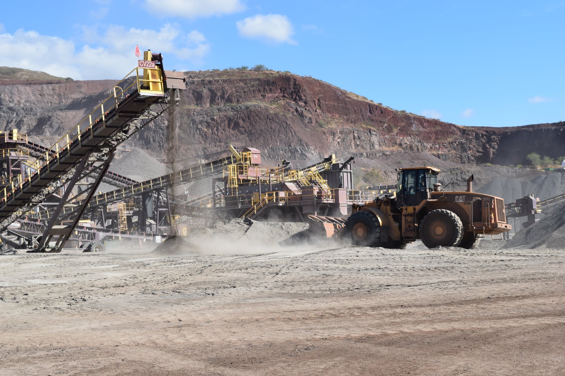 A wheel loader working beside aggregate processing conveyors at a quarry.